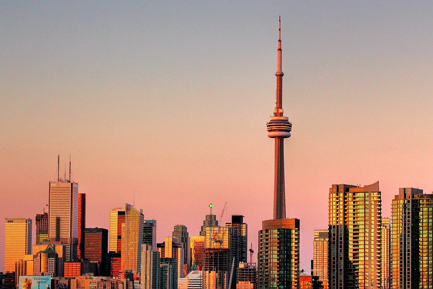 The CN Tower and Toronto waterfront skyline in pink and golden sunset light.