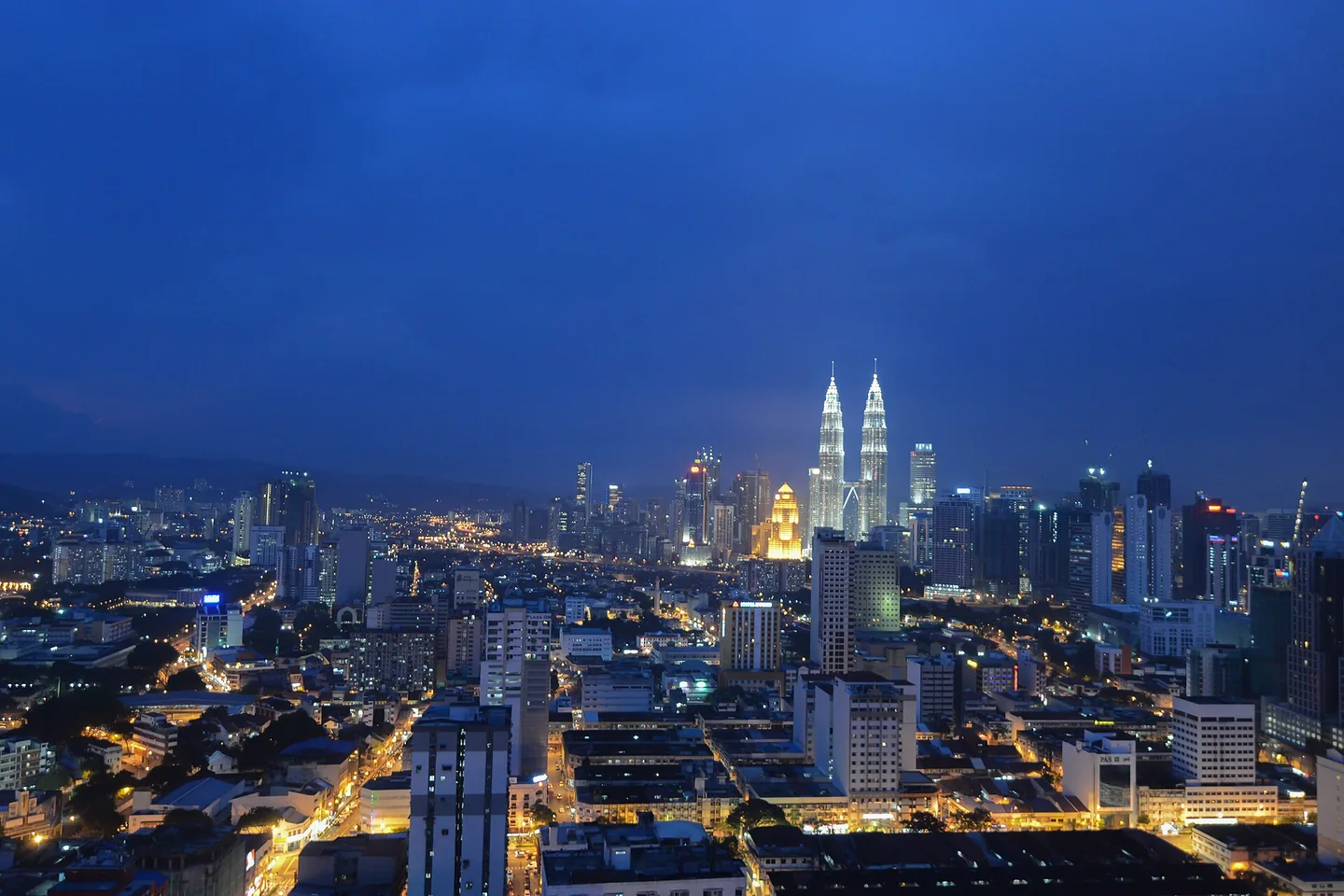 The Petronas Twin Towers rise above Kuala Lumpur’s illuminated streets at blue hour.